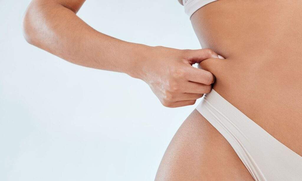 lipo vs tummy tuck person pinching fat on their waist